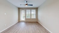This thoughtfully designed two-bedroom, two-bathroom residence in Oviedo, Florida offers a clean, modern aesthetic across a single floor. The open-concept kitchen and living area serves as the heart of the home, with the kitchen showcasing white shaker cabinetry, quartz countertops, a subway tile backsplash, stainless steel appliances including a French door refrigerator and electric range, and a center island with an undermount sink. Light wood-look flooring runs throughout the main living areas, complementing the neutral warm-toned walls. The living room benefits from natural light through large windows with blinds and a sliding glass door leading to an outdoor area, with a ceiling fan overhead. A convenient in-unit stacked washer and dryer is neatly tucked behind a sliding barn door adjacent to the kitchen. The primary bedroom features plush carpet, a walk-in closet, and a ceiling fan, while the second bedroom is equally well-appointed with soft carpet flooring. Both bathrooms are finished in light, neutral tones — one featuring a tub-shower combo with large-format tile surround, and the other with a white vanity, quartz countertop, and wood-framed mirror. Two hallways connect the spaces efficiently, creating a functional and cohesive floor plan.