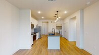 This thoughtfully designed single-floor residence offers a clean, modern aesthetic throughout, centered around an open-concept layout that seamlessly connects the kitchen, dining, and living areas. The kitchen is a standout feature, showcasing white shaker-style cabinetry, dark granite countertops, a subway tile backsplash, and a full suite of stainless steel appliances including a refrigerator, range, and built-in microwave. A centrally positioned island with an undermount sink and stylish pendant lighting serves as the focal point, providing both additional workspace and casual dining potential. Warm-toned hardwood-style flooring flows throughout the main living areas, complementing the bright white walls and recessed lighting overhead. The living room benefits from abundant natural light through large windows with blinds, a ceiling fan, and direct access to an outdoor balcony. The bedroom continues the comfortable feel with plush carpeting, a ceiling fan, and a window that invites natural light. The bathroom is well-equipped with a walk-in glass-enclosed shower featuring white subway tile, a dark granite vanity, white cabinetry, and direct access to a spacious walk-in closet with built-in shelving. A dedicated in-unit laundry area with a full-size washer and dryer and overhead shelving adds everyday convenience to this well-appointed residence.