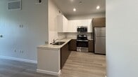 This 420-square-foot single-floor studio apartment is located on E Apache Blvd in Tempe, AZ 85281, offering a well-designed layout that maximizes functionality within a compact footprint. The kitchen is a standout feature, showcasing a contemporary two-tone cabinet design with sleek white upper cabinets and warm wood-grain lower cabinets. Light granite countertops provide ample prep space, while a white subway tile backsplash adds a clean, modern aesthetic. The kitchen is fully equipped with stainless steel appliances, including a gas range, over-the-range microwave, refrigerator, and dishwasher, along with an undermount sink. Light wood-tone luxury vinyl plank flooring runs throughout the kitchen and living areas, creating a cohesive and easy-to-maintain surface. The living area is open and airy, featuring neutral gray walls, recessed lighting, and a ceiling fan. The bathroom is efficiently designed with wood-grain cabinetry, a vanity with a light countertop, and a walk-in shower enclosed by white vertical subway tile. Wood-look flooring continues into the bathroom, tying the space together. This unit offers a clean, modern interior well-suited for single occupants or students near Arizona State University.