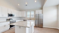 Located at 2909 Shoals Point Way in Leland, NC, this single-story, 3-bedroom, 2-bathroom home offers a clean, modern aesthetic with consistent finishes throughout. The open-concept kitchen and living area serves as the heart of the home, featuring vaulted ceilings with recessed lighting that enhance the sense of space. The kitchen is appointed with crisp white shaker-style cabinetry, granite countertops, a central island with additional granite workspace, and a full suite of stainless steel appliances including a range, microwave, dishwasher, and French door refrigerator. Wood-look plank flooring runs throughout the main living areas and bedrooms, providing a cohesive and low-maintenance finish. The primary bedroom includes vaulted ceilings, a ceiling fan, and closet storage. Additional bedrooms are bright and well-proportioned, with large windows allowing generous natural light and neighborhood views. The primary bathroom features a walk-in glass shower and a white vanity with granite countertops, while the secondary bathroom includes a full tub-shower combo. Neutral wall tones and white trim create a clean, move-in ready environment throughout this efficiently designed home.