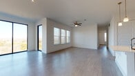 This single-story home showcases a clean, modern design with wood-look flooring and crisp white walls throughout. The spacious main living area is bright and open, benefiting from large sliding glass doors and windows fitted with blinds that invite natural light and outdoor views. A ceiling fan overhead and track lighting add functional detail to the airy space.

The kitchen is well-appointed with a large central island featuring a quartz countertop and undermount sink, complemented by gray flat-front cabinetry, a marble-style tile backsplash, and a full suite of stainless steel appliances including a refrigerator with ice maker, range, microwave, and dishwasher.

The bedrooms are generously sized, each with ceiling fans and wood-look flooring. One bedroom includes a walk-in closet with built-in shelving. The bathrooms are finished to a high standard: one features a tiled tub-shower combination with light wood-look tile flooring, while another offers a glass-enclosed walk-in shower and a vanity with quartz countertops and gray cabinetry. A third bathroom includes a wide quartz vanity counter and a tiled shower. The overall ambiance is bright, contemporary, and move-in ready.