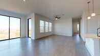 This single-story home showcases a clean, modern design with wood-look flooring and crisp white walls throughout. The spacious main living area is bright and open, benefiting from large sliding glass doors and windows fitted with blinds that invite natural light and outdoor views. A ceiling fan overhead and track lighting add functional detail to the airy space.

The kitchen is well-appointed with a large central island featuring a quartz countertop and undermount sink, complemented by gray flat-front cabinetry, a marble-style tile backsplash, and a full suite of stainless steel appliances including a refrigerator with ice maker, range, microwave, and dishwasher.

The bedrooms are generously sized, each with ceiling fans and wood-look flooring. One bedroom includes a walk-in closet with built-in shelving. The bathrooms are finished to a high standard: one features a tiled tub-shower combination with light wood-look tile flooring, while another offers a glass-enclosed walk-in shower and a vanity with quartz countertops and gray cabinetry. A third bathroom includes a wide quartz vanity counter and a tiled shower. The overall ambiance is bright, contemporary, and move-in ready.