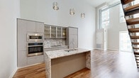 Located in the heart of Detroit at 313 Park St, this thoughtfully designed two-story residence offers three bedrooms, two bathrooms, and generous living space spread across two floors. The main level immediately impresses with dramatic double-height ceilings, floor-to-ceiling windows, and large sliding glass doors that bathe the open living area in natural light while framing striking views of the Detroit skyline. A standout granite-surround fireplace anchors the living room, complemented by warm hardwood flooring throughout. Exposed industrial-style ductwork adds an urban loft character to the space. The upper level hosts carpeted bedrooms, including a well-sized primary bedroom featuring a walk-in closet and a sliding door with direct balcony access and city views. Additional bedrooms offer large windows with urban vistas and hardwood flooring. Both bathrooms are finished to a high standard, featuring granite-topped vanities, vessel or undermount sinks, backlit mirrors, and tiled tub-shower combinations with elegant chevron-patterned tile flooring. A hallway and two closets complete the layout, ensuring practical storage throughout. The two-floor layout provides a clear distinction between living and sleeping areas, making this urban residence both functional and visually impressive.