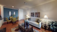 This single-story residence in Humble, TX (77396) offers a thoughtfully designed layout that balances comfort and functionality. The living room serves as the heart of the home, featuring warm hardwood-style flooring, elegant crown molding, and a large window dressed with patterned curtains that invite generous natural light. A glass-top coffee table and plush sofa create an inviting gathering space, while a dedicated dining area with yellow-green chairs and a teal accent wall adds a vibrant touch nearby. The kitchen is outfitted with rich wooden cabinetry extending to the ceiling, dark granite-style countertops, a stainless steel sink, and a full suite of black appliances including a refrigerator, electric range, and built-in microwave — offering ample storage and a practical workspace. The bedroom is carpeted for comfort, featuring a ceiling fan, large windows with outdoor views of surrounding greenery, built-in shelving, and room for a dedicated workspace. An adjoining bathroom includes a full tub-shower combination with tile surround, and direct access to a spacious walk-in closet with multi-tier wire shelving. Throughout the home, crown molding and neutral tones contribute to a cohesive, polished ambiance.