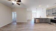 This single-story, 2-bedroom, 2-bathroom home offers a thoughtfully designed open-concept layout that seamlessly connects the living, dining, and kitchen areas. Durable light-toned luxury vinyl plank flooring runs throughout the main living spaces, while plush carpet adds comfort to the bedrooms. The kitchen is a standout feature, equipped with gray shaker-style cabinetry, a tile backsplash, white countertops, a full suite of stainless steel appliances including a refrigerator, range, microwave, and dishwasher, and pendant lighting above the kitchen island. Ceiling fans are installed in the living area and bedrooms, contributing to both comfort and airflow. The primary bedroom is generously sized, featuring carpeted flooring and access to a dedicated closet. The second bedroom also includes carpeted flooring and a louvered closet door. Both bathrooms are well-appointed, with one featuring a tub-shower combination with tiled surround and built-in shelving. Additional storage is provided through two closets, including a walk-in with wire shelving. The home's neutral color palette and clean finishes create a bright, modern ambiance throughout.