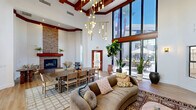 Located at 901 E Van Buren St in Phoenix, AZ, this thoughtfully designed single-floor space makes a striking impression with its dramatic, soaring ceilings accented by bold red-painted exposed beams that add warmth and architectural character. The open living area is anchored by a floor-to-ceiling stacked-stone fireplace, serving as a stunning focal point that blends rustic and contemporary aesthetics seamlessly.

Light hardwood flooring runs throughout, complementing the crisp white walls and creating an airy, welcoming atmosphere. Large floor-to-ceiling windows and a glass-paneled entryway flood the interior with abundant natural light and offer views to the outdoors. A stylish media wall features vertical wood slat paneling, built-in cabinetry with arched detailing, and trailing greenery cascading overhead, adding a lively, organic element to the space.

The living area is furnished with a mix of curated seating, layered rugs with traditional patterns, and a large dining table with woven chairs, making the space well-suited for both relaxed gatherings and communal use. Potted plants and decorative foliage are thoughtfully placed throughout, enhancing the natural, earthy ambiance. An elegant globe pendant chandelier adds a refined finishing touch to this vibrant and inviting interior.