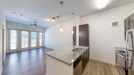 Located at 2604 Aldrich Street in Austin, TX, this one-bedroom, one-bathroom residence offers a thoughtfully designed single-floor layout with a clean, modern aesthetic. The open-concept living and kitchen area serves as the heart of the home, anchored by a granite-topped island with a built-in sink and pendant lighting overhead. Dark espresso cabinetry provides ample storage, complemented by a full suite of stainless steel appliances including a refrigerator, range, microwave, and dishwasher. Hardwood-style flooring runs throughout the main living areas, while track lighting and a ceiling fan add both function and style. Large glass doors at the end of the living area flood the space with natural light and offer views of the surrounding greenery. A carpeted hallway leads to the private bedroom, which features plush carpet flooring and a window with outdoor views, creating a calm retreat. The walk-in closet offers multi-tier wire shelving for organized storage. The bathroom includes a framed glass-enclosed walk-in shower, wood-look flooring, and dark vanity cabinetry. This residence combines practical functionality with contemporary finishes in a prime Austin location.