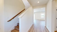 This two-story home presents a clean, contemporary design with a neutral color palette of crisp whites and warm wood tones carried consistently throughout both levels. The main floor features an open-concept layout, as seen in the 3D floor plan, with a well-appointed kitchen at its heart. The kitchen is equipped with stainless steel appliances, wood-grain cabinetry extending to the ceiling, white quartz countertops, and a sizeable center island—all complemented by light hardwood-style flooring and multiple windows that bring in natural light and outdoor views. A convenient half-bath on the main level features wood-look LVP flooring, a window for natural light, and matte black hardware accents.

A staircase with a warm wood handrail and white balustrade connects the floors, leading to the upper level where carpeted bedrooms offer a comfortable, quiet retreat. Each bedroom includes neutral walls and windows overlooking the surroundings. The primary bathroom impresses with a dual-sink vanity featuring white cabinetry, quartz countertops, a glass-enclosed walk-in shower with subway tile, and light hardwood flooring. A secondary full bathroom includes a single vanity and a tub-shower combination, finished in a bright, clean aesthetic.
