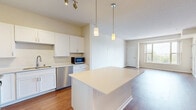 Located at 7475 Flying Cloud Dr in Eden Prairie, MN, this one-bedroom, one-bathroom residence offers a well-designed, single-floor layout that maximizes comfort and functionality. The open-concept kitchen and living area form the heart of the home, creating a seamless flow between spaces. The kitchen is outfitted with crisp white cabinetry, stainless steel appliances including a refrigerator, range, dishwasher, and microwave, and a central island with a light countertop that provides additional prep and seating space. Pendant lighting and a track light fixture add a modern touch overhead. Warm hardwood-style flooring runs throughout the main living areas, complementing the neutral, light-toned walls. The living room is bright and open, benefiting from large windows and a glass-paned door that leads to a private balcony with outdoor views. The bedroom is generously sized, featuring its own large window with tree-lined views, and includes a spacious walk-in style closet with built-in shelving. The bathroom is thoughtfully appointed with a full tub and shower combination, accessory grab bars for added accessibility, and a clean white vanity. The textured ceiling and consistent flooring tie the residence together with a cohesive, move-in-ready aesthetic.