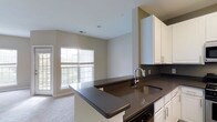 Located at 900 Reisling Lane in West Chester, PA, this single-floor residence offers a thoughtfully designed open-concept layout that seamlessly connects the kitchen and living areas. The kitchen is outfitted with crisp white cabinetry, sleek dark countertops, and a stainless steel undermount sink, creating a striking contrast that gives the space a modern, polished aesthetic. A peninsula-style counter extends into the living area, providing additional workspace and a natural gathering point. The living area is bright and airy, benefiting from a large multi-pane window and a glass door that bathe the space in natural light while offering views of the outdoor surroundings. Light-colored carpeting throughout the living area adds warmth and comfort underfoot. Neutral wall tones and clean lines throughout contribute to a calm, welcoming ambiance. The single-floor layout ensures easy accessibility and a cohesive flow between spaces, making everyday living both practical and comfortable. This residence in West Chester, PA combines functional design with contemporary finishes for a refined and inviting living experience.