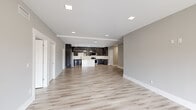 This single-story space offers a thoughtfully designed open-concept layout with a generous footprint spread across seven rooms. The interior is unified by light-toned hardwood-style flooring that runs continuously throughout, complementing the neutral gray wall palette and crisp white baseboards to create a clean, contemporary aesthetic.

The standout feature is the kitchen, which is equipped with floor-to-ceiling dark wood-grain cabinetry accented by sleek chrome hardware. A large waterfall-edge quartz island serves as the centerpiece, beneath modern circular pendant lighting. Stainless steel appliances, including a refrigerator, range, microwave, and dishwasher, add a professional finish, while recessed lighting illuminates the space throughout.

The open living area flows seamlessly from the kitchen, offering a spacious and versatile layout. Private rooms feature sliding windows that invite natural light and outdoor views, each fitted with a modern black ceiling fan. One room includes direct access to a dedicated bathroom finished with polished marble-style tile flooring, matching wall surrounds in the walk-in shower, and refined, minimalist fixtures. The overall ambiance is modern, bright, and move-in ready.