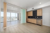 This well-designed one-bedroom, one-bathroom residence at 1140 S Normandie Ave in Los Angeles offers a thoughtfully efficient layout with modern finishes throughout. Light-toned wood-style flooring runs seamlessly across the entire unit, complementing the bright, neutral color palette that gives the space an open and airy feel.

The combined kitchen and living area serves as the heart of the unit. The kitchen is outfitted with flat-front light wood cabinetry, stainless steel appliances including a refrigerator, range, microwave, and dishwasher, and a striking dark tile backsplash that adds contrast and visual interest. White quartz-style countertops complete the contemporary look.

The living area opens directly onto a private balcony through expansive floor-to-ceiling sliding glass doors, flooding the space with abundant natural light and offering open views of the surrounding Los Angeles neighborhood, with palm trees visible in the distance.

The bedroom is a clean, minimalist space with ample room and access to two closets, providing generous storage. The bathroom features a light wood vanity with an undermount sink, white countertop, matte black fixtures, and a framed mirror with built-in storage. A dedicated laundry area with a stacked washer and dryer adds everyday convenience. The entrance hallway connects all rooms efficiently, making the layout feel intuitive and functional.
