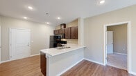 This single-floor residence offers a practical and thoughtfully designed layout, accommodating two bedrooms and two full bathrooms within a comfortable footprint. The open-concept kitchen serves as a central hub, featuring rich dark-brown cabinetry, marble-look countertops, a peninsula with an integrated sink, and a full suite of black appliances including a refrigerator, range, microwave, and dishwasher. The kitchen flows seamlessly into the living area, which is finished with warm wood-look flooring and a sliding glass door that invites natural light into the space.

The bedrooms are carpeted for comfort and each includes windows with blinds, providing natural light and privacy. The primary bedroom connects to a dedicated closet outfitted with wire shelving and hanging rods, offering generous organizational storage. Both bathrooms are finished consistently with the kitchen aesthetic, featuring dark-wood vanities, marble-look countertops, well-lit vanity mirrors, and chrome hardware accents.

A carpeted hallway connects the bedrooms and bathrooms, contributing to a cohesive and quiet private wing. Throughout the residence, neutral warm-beige walls, recessed lighting, and clean white trim create a bright, move-in-ready ambiance that is both modern and inviting.