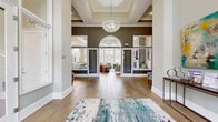 Located at 100 Dalton Ln in Charlottesville, VA, this thoughtfully designed single-floor space offers a generous and open layout ideal for gathering and relaxation. The grand entryway immediately sets the tone with soaring coffered ceilings, warm hardwood flooring, and a striking crystal chandelier suspended above. A bold dark accent wall frames a series of glass-paneled French doors with an elegant arched transom, seamlessly connecting the foyer to the adjoining rooms and flooding the space with natural light.

The kitchen is both functional and refined, featuring rich dark wood cabinetry, crisp white quartz countertops, stainless steel appliances including a full-size refrigerator, and a large island with leather bar stools. Tiered pendant lighting adds a contemporary elegance, while large windows offer views of the outdoors.

The living area is anchored by a stacked stone fireplace with a wood mantel and wall-mounted television, creating a warm and inviting focal point. Built-in bench seating with cushions and light blue accent chairs add comfort and style. Glazed interior windows connect this lounge area to adjacent rooms, maintaining a sense of openness throughout. The cohesive palette of soft neutrals, cool blues, and natural wood tones gives the entire space a polished, welcoming ambiance.