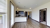 This single-floor space showcases a well-designed open-concept layout that seamlessly connects the kitchen and living areas. The kitchen is a standout feature, equipped with stainless steel appliances, including a microwave and range, complemented by rich dark cabinetry that contrasts elegantly with the light-toned walls. A peninsula with granite countertops and an integrated sink serves as both a functional workspace and a natural divider between the kitchen and the living area, with pendant lighting above adding a refined touch.

Durable hardwood-style flooring runs throughout the space, providing a warm and cohesive aesthetic. The living area is generously sized, offering flexibility for various furniture arrangements. A large sliding glass door along one wall allows natural light to flood the interior, enhancing the bright and airy ambiance.

A hallway visible from the main area leads to additional rooms, suggesting a practical and well-organized floor plan. Recessed and flush-mount ceiling lighting ensures consistent illumination throughout. The overall design balances contemporary finishes with functional living, creating a clean and inviting environment.