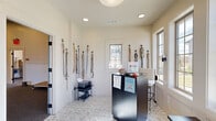 Livano Pet Center in Vestavia Hills, Alabama is a purpose-built pet care facility designed with both functionality and comfort in mind. The single-floor layout encompasses three distinct areas that work together to provide a seamless experience for pets and their owners.

The welcoming reception area features a sleek dark-wood front desk, recessed and pendant lighting, and patterned tile flooring. Leashes and accessories line the crisp white walls, while windows allow natural light to brighten the space and create an inviting first impression.

Beyond reception, a spacious open activity area serves as the heart of the facility. This room boasts notably high ceilings with exposed beam detailing, a two-tone wall treatment with white wainscoting below and neutral paint above, and durable carpet flooring suited for active pets. Large windows offer views of the surrounding outdoor environment, keeping the space bright and airy. A turf relief station is conveniently positioned within this area, and multiple entry doors with windowed panels ensure smooth pet traffic flow.

A dedicated grooming room rounds out the facility, equipped with a professional stainless steel grooming tub, a grooming arm and table, non-slip penny-tile flooring, and charming dog-themed artwork on the walls — combining practicality with a polished aesthetic throughout.