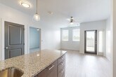 Located at 650 E Elm St in Des Moines, Iowa, this thoughtfully designed one-bedroom, one-bathroom unit offers a clean, modern aesthetic throughout. The open-concept kitchen and living area serves as the heart of the space, anchored by a large granite-topped island with an undermount double sink and stylish pendant lighting. Dark espresso cabinetry, a white tile backsplash, and stainless steel appliances — including a refrigerator, range, and microwave — complete the well-appointed kitchen. Light hardwood-style flooring flows throughout the main living areas, complementing the bright, neutral palette. A ceiling fan with light kit keeps the living room comfortable, which also features access to a generous tiled balcony offering open views of the surrounding area. The bedroom features plush carpeting, a ceiling fan, and a window that fills the room with natural light. The full bathroom includes a granite-topped vanity with dark cabinetry and a full tub/shower combo. A dedicated laundry room with in-unit washer and dryer hookups adds everyday convenience. The space combines modern finishes with functional design for comfortable urban living in Des Moines.