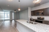This single-floor residence features a thoughtfully designed open-concept layout where the kitchen and living areas flow seamlessly together. The kitchen is a standout space, anchored by a generously sized island topped with speckled granite countertops and equipped with a double stainless steel sink. Pendant lighting illuminates the island, while dark espresso cabinetry, a subway tile backsplash, and stainless steel appliances — including a refrigerator, electric range, and built-in microwave — complete the modern aesthetic. Light hardwood flooring extends throughout the kitchen and living areas, enhancing the bright, open feel. Large windows allow natural light to fill the living space, which also features a ceiling fan.

The bedroom is carpeted for comfort and includes a ceiling fan, ample closet space, and large windows that bring in additional natural light. An adjoining bathroom offers a granite-topped vanity with dark cabinetry, a mirrored medicine cabinet, a combination tub and shower, and light hardwood-style flooring. A dedicated laundry area provides the convenience of an in-unit full-sized washer and dryer. Overall, the space presents a clean, contemporary aesthetic with functional finishes throughout.