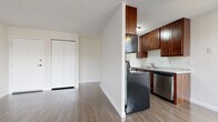 This single-floor unit is thoughtfully laid out to maximize functionality across its living spaces. Hardwood-style laminate flooring runs consistently throughout, lending a cohesive and clean aesthetic to the entire unit.

The kitchen is positioned at one end of the main living area, partially separated by a partial dividing wall that maintains an open feel. It features rich dark-wood cabinetry with ample upper storage, light granite-style countertops, a stainless steel dishwasher, a black range, and a stainless steel refrigerator. A ceiling fan with a light fixture overhead serves the adjacent living and dining area. Baseboard heating runs along the exterior walls, and a wall-mounted air conditioning unit ensures year-round comfort. Windows allow natural light to filter in, offering views of the surrounding neighbourhood.

The bedroom is a well-proportioned space with its own window and baseboard heating. A closet with double bifold doors provides generous storage. The full bathroom is finished in neutral tones and includes a bathtub with shower, a vanity with dark wood cabinetry, and a window for natural ventilation. The unit also features a secondary closet near the entryway, adding practical storage capacity.
