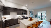 This thoughtfully designed one-bedroom, one-bathroom residence in Spring, TX offers a well-appointed single-floor layout that blends modern style with everyday functionality. The open-concept living and kitchen area serves as the heart of the home, featuring dark shaker-style cabinetry that reaches the ceiling, a white subway tile backsplash, stainless steel appliances including a gas range, and a large central island with quartz countertops and seating — perfect for casual dining or entertaining. Globe pendant lights add a contemporary touch overhead, while light wood-style flooring flows throughout the main living areas. The living room is bright and inviting, anchored by a sliding glass door that opens onto a private balcony with outdoor seating, filling the space with natural light. The bedroom is a calm retreat, outfitted with plush carpet, a ceiling fan, and large windows that frame outdoor views. The full bathroom is generously proportioned, featuring a wide vanity with ample storage, wood-style flooring, and direct access to a dedicated walk-in closet with built-in shelving. Clean white walls, recessed lighting, and high ceilings throughout contribute to an airy, modern ambiance that defines this well-crafted residence.