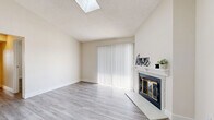 Located at 8293 W Floyd Ave in Lakewood, Colorado, this single-floor, 2-bedroom, 2-bathroom home offers a clean, modern aesthetic with light wood-look flooring and neutral tones throughout. The open living room is a standout feature, highlighted by a skylight that floods the space with natural light, a glass-door fireplace with a white mantel, and a sliding glass door fitted with vertical blinds that provides outdoor access and additional brightness. The kitchen is efficiently designed in a galley layout, featuring white cabinetry with contemporary hardware, white quartz countertops, a stainless steel dishwasher, and a refrigerator — all complemented by a ceiling fan overhead. A stacked in-unit washer and dryer is conveniently tucked within the kitchen area. Both bedrooms are well-proportioned with ample closet space; the generously sized primary bedroom offers comfortable accommodation. The two bathrooms are clean and functional — one features a dual-sink vanity with white cabinetry and a tiled shower, while the second includes a full tub/shower combination. Textured ceilings are consistent throughout the home. A hallway connects the rooms, and two closets provide additional storage throughout the residence.