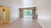 Located at 2401 Arlington Blvd in Charlottesville, VA, this single-floor residence offers three bedrooms and one bathroom across a well-organized layout. Wood-look laminate flooring runs consistently throughout every room, giving the home a cohesive, clean aesthetic. The living room is the largest space in the unit, featuring neutral walls, bright lighting, and a sliding glass door that opens to a private balcony overlooking lush greenery — a standout feature that brings natural light and outdoor views into the home. The galley-style kitchen is efficiently designed with warm oak cabinetry, light countertops, a stainless steel sink, a dishwasher, and a window that allows natural light to filter in. The three bedrooms are each finished with the same laminate flooring and neutral tones. The primary bedroom is generously sized and includes a dedicated closet with a hanging rod. Additional bedrooms feature sliding closet doors and windows with wooded views. A dedicated walk-in closet with full-length rod storage adds to the home's organizational capacity. The bathroom includes a full tub-shower combination with a decorative curtain, toilet, and easy-care finishes. A connecting hallway ties all rooms together, making for a functional and straightforward floor plan throughout.
