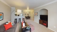 This single-floor residence offers a thoughtfully designed open-concept layout that seamlessly connects the living, dining, and kitchen areas. The spacious living room features plush wall-to-wall carpeting, crown molding, and large windows that flood the space with natural light, creating a bright and welcoming atmosphere. A breakfast bar with seating bridges the kitchen to the main living area, enhancing the sense of openness and flow.

The kitchen is well-equipped with light wood cabinetry, white appliances including a range, microwave, dishwasher, and refrigerator, along with light-toned countertops and tile flooring. The adjacent dining area provides ample room for a full dining set and is accented by a pendant light fixture and vibrant wall art.

The primary bedroom is a comfortable retreat, featuring a ceiling fan, carpeted floors, a built-in shelving nook, and a walk-in closet. A second bedroom offers generous proportions with large windows that bring in abundant natural light, crown molding, and soft carpeting. The full bathroom is well-appointed with a single-sink vanity, a soaking tub with shower, and light wood cabinetry for storage. An arched hallway entry adds a refined architectural detail to the overall design.