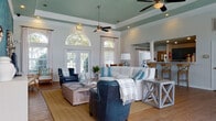 Located at 4911 Signature Dr in Myrtle Beach, SC, this single-floor community clubhouse showcases a thoughtfully designed coastal aesthetic throughout. The entrance welcomes visitors with a tray ceiling accented in muted teal, a striking coral-branch chandelier with a gold finish, warm hardwood flooring, and a patterned navy area rug — setting an inviting tone from the moment you step inside.

The main lounge is an expansive, light-filled gathering space defined by soaring tray ceilings painted in a soft sage green, dual ceiling fans, and generous arched windows paired with French doors that flood the room with natural light and outdoor views. Comfortable seating arrangements, coastal-themed décor, and decorative columns add architectural character to the space.

A dining nook adjacent to the lounge features a round white pedestal table surrounded by wicker chairs beneath an elegant arched window. The supporting kitchen area offers teal cabinetry, stainless steel appliances, and hardwood flooring, complemented by nautical artwork.

A dedicated sitting area features bold blue textured wallpaper and curated coastal art, providing a relaxed retreat. The fitness center is well-appointed with treadmills, ellipticals, stationary bikes, free weights, medicine balls, wall-mounted televisions, and rubberized flooring — with a mirror wall and natural light enhancing the workout environment.
