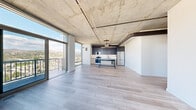 Located at 1522 Gordon Street in Los Angeles, this three-bedroom, two-bathroom residence showcases an industrial-modern aesthetic across a single thoughtfully designed floor. Exposed concrete ceilings with visible ductwork and structural columns establish a bold architectural character throughout, complemented by light-toned hardwood flooring that runs seamlessly from room to room.

The open-concept living and kitchen area is a standout, anchored by dramatic floor-to-ceiling windows and sliding glass doors that open to a balcony, framing sweeping panoramic views of the Los Angeles skyline and surrounding mountain ranges. The kitchen features dark navy cabinetry, white subway tile backsplash, stainless steel appliances, and a central island with bar seating — ideal for both cooking and entertaining.

The bedrooms are bright and airy, with several rooms benefiting from the same expansive window system, offering elevated city views and abundant natural light. The primary bedroom provides a comfortable and private retreat.

Both bathrooms are finished in a clean, contemporary style with floor-to-ceiling white subway tile, glass-enclosed tub-shower combinations, matte black fixtures, floating wood vanities, and round mirrors. One bathroom conveniently incorporates an in-unit stacked washer and dryer. A wide hallway connects all areas, maintaining an open and functional flow throughout the residence.