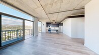 Located at 1522 Gordon Street in Los Angeles, this three-bedroom, two-bathroom residence showcases an industrial-modern aesthetic across a single thoughtfully designed floor. Exposed concrete ceilings with visible ductwork and structural columns establish a bold architectural character throughout, complemented by light-toned hardwood flooring that runs seamlessly from room to room.

The open-concept living and kitchen area is a standout, anchored by dramatic floor-to-ceiling windows and sliding glass doors that open to a balcony, framing sweeping panoramic views of the Los Angeles skyline and surrounding mountain ranges. The kitchen features dark navy cabinetry, white subway tile backsplash, stainless steel appliances, and a central island with bar seating — ideal for both cooking and entertaining.

The bedrooms are bright and airy, with several rooms benefiting from the same expansive window system, offering elevated city views and abundant natural light. The primary bedroom provides a comfortable and private retreat.

Both bathrooms are finished in a clean, contemporary style with floor-to-ceiling white subway tile, glass-enclosed tub-shower combinations, matte black fixtures, floating wood vanities, and round mirrors. One bathroom conveniently incorporates an in-unit stacked washer and dryer. A wide hallway connects all areas, maintaining an open and functional flow throughout the residence.