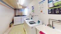 Located at 262 Rose St in Barrie, Ontario, this shared laundry facility is a well-organized, single-floor utility space designed for communal use. The room is efficiently laid out to accommodate multiple top-loading washing machines and front-loading dryers, providing ample capacity for residents. A utility sink is also present, offering added convenience for hand-washing or pre-treating garments.

The space features distinctive yellow-green mosaic tile flooring throughout, which adds a subtle visual character to the otherwise clean and functional interior. The walls are finished in a soft, neutral tone, contributing to a bright and tidy atmosphere. Ventilation is addressed through wall-mounted HVAC grilles, and an electrical panel is accessible along one wall.

Natural light enters through a window, supplemented by overhead fluorescent lighting to ensure the space remains well-lit at all times. Instructional signage for proper washer and dryer usage is posted on the walls, making the facility straightforward to navigate. Floor drains are integrated into the tile layout, reflecting a practical approach to maintenance and cleanliness. The overall design prioritizes functionality and ease of use, making this a reliable shared amenity.