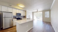 This two-floor residence offers a thoughtfully designed layout that blends functionality with comfortable living. The open-concept kitchen serves as the heart of the home, featuring crisp white cabinetry, a grey tile backsplash, light quartz countertops, and a full suite of stainless steel appliances including a refrigerator, electric range, and over-the-range microwave. A peninsula with an integrated sink extends the counter space and creates a natural divide between the kitchen and the adjoining living area. The living space is finished with wood-look flooring and benefits from generous natural light streaming through sliding glass doors fitted with vertical blinds, offering views of the surrounding greenery. Ceiling fans are present throughout the home, providing consistent airflow across all rooms. The bedrooms are carpeted for comfort, with neutral tones and multiple windows dressed with horizontal blinds that allow for ample natural light. At least one bedroom features a walk-in closet, offering practical storage. The bathroom is cleanly finished with a white vanity, quartz-style countertop, and a tub-shower combination. Crown molding accents select rooms, adding a refined architectural detail to the overall interior.