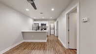 This single-floor unit is designed with a clean, contemporary aesthetic, featuring neutral gray walls, crisp white trim, and wood-look vinyl plank flooring that runs consistently throughout the space, creating a cohesive and well-maintained appearance.

The kitchen serves as a central highlight, outfitted with white shaker-style cabinetry, white quartz countertops, and a full suite of stainless steel appliances including a refrigerator, electric range, and over-the-range microwave. A mosaic tile backsplash adds a subtle decorative element behind the range. A peninsula with an undermount sink extends into the living area, providing additional counter space and a natural transition between the kitchen and the main living zone. Recessed lighting and a ceiling fan overhead ensure the area is well-lit and ventilated.

The bedrooms are comfortably sized, each featuring wood-look flooring, neutral walls, and windows fitted with horizontal blinds that allow for natural light control. One bedroom includes a ceiling fan for added comfort.

The bathroom is finished with large-format white wall tiles surrounding a soaking tub and tub/shower combination, complemented by matte black fixtures that provide a modern contrast. A dedicated in-unit laundry area with a stacked washer and dryer is conveniently accessible from the main hallway.