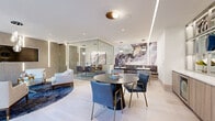 Located at 118 Park Ave in Rutherford, NJ, this single-floor amenity space delivers a refined, contemporary design with carefully curated details throughout. The open layout is anchored by light hardwood flooring and crisp white ceilings with sleek linear LED lighting that runs throughout, lending the space a polished, modern ambiance.

A standout feature is the glass-enclosed private meeting room, finished with textured herringbone wall panels and vertical LED accent lighting. Inside, a glass-top conference table surrounded by plush velvet chairs creates an elegant yet functional setting. Adjacent to the meeting room, a comfortable lounge area offers cream upholstered armchairs arranged around a contemporary coffee table, with large black-framed windows providing views of the surrounding neighborhood.

A striking banquette dining area features built-in seating set against a dramatic abstract mural wall in deep purples and gold tones, complemented by pendant lighting overhead and small café-style tables. A round black dining table with navy blue leather chairs occupies the central area of the space, with a vibrant patterned area rug adding depth and color.

A service bar or kitchenette area with warm wood cabinetry and blue bar seating provides additional utility. A full-glass entry door with black framing opens directly to an outdoor walkway, enhancing the connection between the interior and the exterior environment.