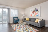 This single-floor residence offers a thoughtfully arranged layout that connects living, dining, and kitchen areas in a functional flow. A hallway entry leads into the living room, which features dark wood-style flooring, a textured ceiling, and a window with access to an outdoor balcony, allowing natural light to fill the space. The living area is generously proportioned, providing ample room for seating arrangements centered around a glass coffee table.

Adjacent to the living room, a compact dining nook accommodates a round table and is brightened by a window overlooking the outdoors. The kitchen is positioned nearby and features white cabinetry, a coil-top electric range, laminate countertops, a built-in sink, and a full-size refrigerator, all within an efficient U-shaped layout.

The residence includes two bedrooms, each finished with plush carpeting and windows that bring in natural light. The primary bedroom offers generous wall space, while the second bedroom includes a sliding-door closet for additional storage. The bathroom features wood-style flooring, a single-sink vanity with white cabinetry, and a tub-shower combination with a curtain enclosure.