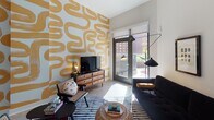 Located in the heart of Washington, DC's vibrant H Street corridor, this single-floor residence offers a thoughtfully designed layout with contemporary finishes throughout. The open kitchen is a standout feature, outfitted with slate-gray cabinetry, stainless steel appliances, white quartz countertops, a central island with bar seating, and light wood flooring — all beneath soaring ceilings with recessed lighting and a stylish pendant fixture. The living area is bright and inviting, anchored by large glass doors that open to a private balcony overlooking the surrounding neighborhood, flooding the space with natural light. A bold accent wall featuring a golden abstract mural adds an artistic focal point, complemented by a secondary sitting nook dressed in dramatic geometric wallpaper for added personality. The bedroom is serene and well-proportioned, with tall ceilings, a large window with neighborhood views, and light wood floors. The bathroom features large-format tile flooring, a vanity with dark countertops, and a full tub-shower combination. Throughout the residence, high ceilings and clean white walls create an airy, modern ambiance with distinct artistic character.