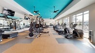 Located at 2554 Davis Rock Dr in Dacula, Georgia, this well-appointed fitness center offers a generously sized, single-floor exercise space designed to accommodate a comprehensive workout experience. The room's most distinctive architectural feature is its bold teal ceiling accent, which contrasts sharply against the crisp white walls and adds a vibrant, energizing atmosphere to the space. Ceiling fans are mounted throughout to ensure comfortable air circulation during workouts.

Large windows line the walls on multiple sides, flooding the interior with abundant natural light and providing open views of the surrounding outdoor areas. The flooring features a durable, multi-toned tile pattern in neutral tones of tan and gray, offering both resilience and visual interest.

Equipment is thoughtfully arranged to maximize the use of the space. A dedicated cardio zone houses a row of TRUE-brand treadmills and elliptical machines, while spin bikes are positioned to take advantage of the natural light. The strength training area includes a full cable machine system, a multi-functional rack, barbells with weight plates, and an extensive dumbbell rack ranging across multiple weights. Adjustable benches and a stability ball round out the free weights section. Full-length mirrors along one wall enhance the sense of openness and allow users to monitor their form. The space also benefits from recessed lighting and a wall-mounted television for entertainment.