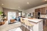 This single-floor residence offers a thoughtfully designed open-concept layout that seamlessly connects the kitchen, dining, and living areas. The kitchen is a functional centerpiece, featuring rich warm-toned cabinetry, white quartz countertops, stainless steel appliances including a refrigerator, range, microwave, and dishwasher, and a spacious island with bar seating — ideal for casual dining or entertaining. Wood-look flooring grounds the kitchen and flows into the main living space.

The living area is generously sized, filled with natural light from large sliding glass doors that open to a private balcony, offering views of the surrounding exterior. A carpeted secondary living or dining area provides additional flexible space, accented by neutral walls and ample room for various furniture arrangements.

The bedrooms are comfortably scaled, each featuring plush carpeting, large windows that invite natural light, and ceiling fans for added comfort. The primary bedroom includes a walk-in closet outfitted with wire shelving and hanging storage for organized living. The bathroom features wood-look tile flooring, a vanity with ample counter space, and a shower with a decorative curtain. Throughout the residence, a consistent neutral color palette and recessed lighting create a calm, modern ambiance.