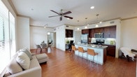 This single-floor residence showcases an open-concept layout that seamlessly connects the living, dining, and kitchen areas into one cohesive and functional space. Warm hardwood flooring extends throughout, providing a consistent and inviting foundation that ties the various zones together.

The kitchen is a standout feature, outfitted with rich dark wood cabinetry, granite countertops, and stainless steel appliances including a refrigerator, range, and microwave. A peninsula with bar-height seating accommodates several stools, making it an ideal spot for casual dining or entertaining. Pendant lighting above the peninsula adds focused illumination and a contemporary aesthetic.

Adjacent to the kitchen, a built-in desk area with open shelving offers a dedicated workspace. The dining area nearby provides a defined space for more formal meals, while the living room is anchored by a ceiling fan that enhances both comfort and air circulation. Recessed and track lighting throughout ensures the space remains well-lit. The open sightlines and thoughtful layout create a bright, airy atmosphere well-suited for modern living.