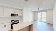 This thoughtfully designed one-bedroom, one-bathroom residence offers a bright and contemporary living experience across a single main floor. The open-concept layout connects the kitchen and living area seamlessly, creating an efficient yet comfortable flow throughout the space.

The kitchen is a standout feature, outfitted with white shaker cabinetry, a white subway tile backsplash, a light stone countertop island, and a full suite of stainless steel appliances including a gas range, built-in microwave, dishwasher, and refrigerator. Light wood-tone flooring runs throughout the main living areas, enhancing the clean, modern aesthetic.

The bedroom is a calm retreat, featuring plush carpet, a ceiling fan, and a window that invites natural light and outdoor views. It connects directly to a spacious walk-in closet equipped with built-in shelving and dual hanging rods, providing ample and organized storage.

The bathroom continues the modern palette with a stone-topped vanity, undermount sink, and large mirror framed by clean white cabinetry.

A private balcony extends the living space outdoors, offering sweeping views of a resort-style pool, palm-lined courtyard, and a dramatic mountain backdrop under open skies — completing this well-appointed modern residence.