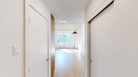 Located at 1090 Rue De Bleury in the heart of downtown Montréal, this efficiently designed single-floor unit offers a thoughtfully laid-out living space with a clean, modern aesthetic. The open-plan layout maximizes every square metre, creating a sense of openness that belies its compact footprint.

A standout architectural feature is the exposed concrete ceiling, which lends an industrial character that contrasts beautifully with the warm light hardwood flooring found throughout the main living area. A large window floods the space with natural light and frames views of the surrounding urban cityscape, further enhancing the airy feel of the interior.

The kitchen is well-appointed with white cabinetry accented by warm wood paneling, a classic subway tile backsplash, and a full suite of stainless steel appliances including a refrigerator, oven, and built-in microwave. The seamless integration of the kitchen into the open living area makes the space ideal for both everyday living and entertaining.

The bathroom is finished to a high standard, featuring a corner glass-enclosed shower, a wall-mounted vanity with a sleek white countertop and modern brushed-chrome fixtures, and a frameless illuminated mirror. Neutral tile flooring and crisp white walls give the bathroom a clean, contemporary look.

Throughout the unit, white walls, consistent finishes, and a minimalist design approach create a cohesive and inviting atmosphere in the heart of Montréal.