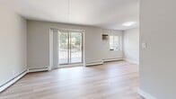Located at 1086 West King Road in Malvern, PA, this one-bedroom, one-bathroom unit offers a well-designed, functional layout across a single floor. The open-concept kitchen and living area serves as the heart of the home, featuring updated white shaker cabinetry, quartz countertops, a subway tile backsplash, and stainless steel appliances including a refrigerator, electric range, and over-the-range microwave. A peninsula with an integrated sink adds prep space and visual separation from the living area. Light wood-style flooring flows throughout the kitchen and living spaces, complementing the neutral gray and white color palette. The living room is generously proportioned, filled with natural light from large windows and a sliding glass door that opens to an outdoor balcony with tree-lined views. A dedicated hallway connects the main living areas to the private spaces, lined with clean white six-panel doors. The spacious bedroom features wall-to-wall carpet, a wall-mounted air conditioning unit, and two closets offering ample storage. The bathroom includes a full tub and shower combination with white tile surround. Baseboard heating is present throughout the unit, and recessed lighting in the kitchen adds a modern finishing touch.