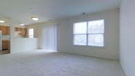 This single-floor space offers a clean, functional layout designed to maximize comfort and usability. The main living area is generously proportioned, featuring soft wall-to-wall carpeting that adds warmth underfoot. Neutral, light-toned walls create a bright and welcoming atmosphere throughout.

Natural light is a defining feature of this space. A large picture window along the exterior wall frames outdoor views and floods the interior with daylight, while vertical blinds on the sliding glass door provide flexible light control and access to the outside. Flush-mounted ceiling lighting supplements the natural illumination, ensuring the space remains well-lit at all hours.

The ceiling is smooth and finished in a clean white, contributing to the open and airy feel of the room. HVAC vents are thoughtfully integrated into both the ceiling and walls, ensuring year-round climate comfort. The overall design is straightforward and unfussy, with a neutral palette that makes the space highly adaptable to a variety of furnishing styles and personal preferences.

The layout provides ample room for multiple functional zones within the living area, offering flexibility in how the space is arranged and utilized. Overall, this space presents a light-filled, move-in-ready environment suited for comfortable everyday living.