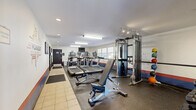 Americana's Gym in Lakewood, Colorado offers a compact yet comprehensive fitness facility thoughtfully designed to maximize functionality. The single-floor layout is divided between a well-equipped exercise room and a dedicated office area.

The exercise room is the centerpiece of the facility, featuring rubber flooring throughout and bright fluorescent lighting overhead. It is outfitted with multiple Matrix-brand treadmills, an elliptical trainer, a stationary bike, and a full cable machine system. Free weight options include a complete rack of dumbbells, kettlebells, and a colorful set of medicine balls. A flat utility bench and adjustable bench support strength training, while a large wall mirror enhances the sense of space. Motivational wall graphics and Americana's Gym signage lend the room an energetic, branded atmosphere. Windows along one wall bring in natural light and offer exterior views.

The office area provides a quieter counterpart to the active fitness space, featuring individual workstation partitions with built-in desk surfaces. A connected lounge nook includes two stylish egg-shaped chairs, a small side table, and recessed lighting, creating a comfortable, welcoming spot for relaxation or check-in. A glass-paneled door with robe storage adds a refined touch to this transitional area.