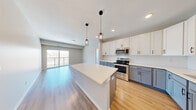 Located at 13944 Edgewood Ave in Savage, MN, this well-appointed 3-bedroom, 2-bathroom single-floor home offers a thoughtfully designed layout with modern finishes throughout. The open-concept kitchen and living area serves as the heart of the home, featuring a large central island with a crisp white countertop, two-tone cabinetry with white upper cabinets and slate-gray lower cabinets, stainless steel appliances, a subway tile backsplash, and stylish geometric pendant lighting. Light hardwood flooring flows through the kitchen and living area, which opens directly to a private balcony through sliding glass doors, filling the space with natural light and outdoor views. The spacious primary bedroom includes sliding glass door access to the balcony and generous proportions, while the additional bedrooms offer plush carpeting, natural light from large windows, and closet storage. A walk-in closet with wire shelving provides ample organization space. The bathrooms are clean and functional, featuring light wood-look flooring, white fixtures, and matte black hardware accents. A dedicated in-unit laundry room houses a full-size washer and dryer. The overall ambiance is bright, modern, and move-in ready.