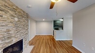 This single-floor residence offers a thoughtfully designed layout that balances comfort and functionality throughout. The open-concept living area immediately draws attention with its warm hardwood-style flooring, a ceiling fan overhead, and a striking stacked-stone accent wall framing a fireplace — providing both visual interest and a cozy focal point. The space flows seamlessly into a pass-through kitchen, which features dark espresso cabinetry, stainless steel appliances including a range, microwave, and refrigerator, and light countertops that contrast elegantly with the cabinetry. The kitchen also provides direct access to a dedicated laundry room equipped with a full-size washer and dryer. The bedrooms are generously sized, finished with plush carpeting and neutral-toned walls, and benefit from natural light streaming through large windows with views of lush greenery. The primary bedroom connects to a well-lit bathroom featuring dark vanity cabinetry, a white countertop, and a bright vanity mirror. A second full bathroom, finished with hardwood-style flooring and a tub-shower combination, serves the remaining living areas. Clean white walls, consistent flooring choices, and a neutral palette throughout lend the space a fresh, move-in-ready appeal.