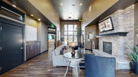 Located at 215 S Conklin Rd in Spokane Valley, WA, this single-story community clubhouse offers a generously sized, multi-functional space designed for both comfort and activity. The main lounge area makes an immediate impression with soaring ceilings, dark hardwood flooring, and a floor-to-ceiling window wall that floods the interior with natural light. A stone-surround fireplace anchors one side of the room, while plush seating arrangements and a wall-mounted display create a welcoming, upscale atmosphere. Adjacent to the lounge, a media room provides a more intimate retreat, featuring patterned carpeting, a large flat-screen TV, and tastefully curated furnishings. The full kitchen is equipped with stainless steel appliances, rich dark cabinetry, a mosaic tile backsplash, and a sweeping granite-topped bar with seating — ideal for entertaining or community events. A secondary lounge area with leather seating and abundant natural light through large windows offers additional gathering space. The fitness center is well-equipped with cardio machines including treadmills and ellipticals, a comprehensive free weight section, exercise benches, stability balls, and wall mirrors, all set on durable rubber flooring with ample natural light from surrounding windows.