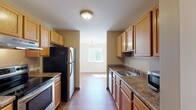 This single-floor residence offers a well-organized layout with distinct living, kitchen, and bedroom areas connected by a practical, open flow. The galley-style kitchen is a functional centerpiece, featuring warm oak cabinetry extending to the ceiling, dark granite-toned countertops, and wood-look flooring. Stainless steel appliances—including a refrigerator, range, and dishwasher—line both sides of the kitchen, which opens toward a dining area illuminated by a chandelier and a large window overlooking greenery.

The living areas are finished with neutral-toned carpet and bright white walls, creating a clean, versatile backdrop. Natural light filters generously through multiple windows, enhancing the airy feel throughout. Each bedroom offers a quiet, carpeted environment with windows that provide outdoor views of surrounding trees.

Two bathrooms are included in the layout. One features wood-look flooring, an oak vanity with a white countertop, and a wide mirror. The second bathroom offers tile flooring and a similarly styled oak vanity. Both are finished in a clean, understated style. Overall, the space presents a practical and cohesive design with consistent warm wood tones and neutral finishes throughout.