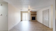 This single-story, 2-bedroom, 1-bathroom unit offers a well-organized layout with wood-look flooring carried consistently throughout every room, complemented by neutral-toned walls and textured ceilings. The combined kitchen and living room forms the heart of the home. The living area is anchored by a striking floor-to-ceiling stone fireplace with a wood mantle and is brightened by a sliding glass door fitted with vertical blinds, allowing ample natural light. A ceiling fan with light kit adds comfort overhead. The kitchen features gray-toned cabinetry, a subway tile backsplash, light countertops, a double sink, and a refrigerator, with a window providing additional natural light. A hallway connects the main living area to the private quarters, where two bedrooms each include ceiling fans and closet access. The primary bedroom benefits from a spacious walk-in closet equipped with built-in shelving and hanging rods. The second bedroom features a bright window and a mirrored closet door. The full bathroom is appointed with a tiled tub-shower combination and wood-look flooring. A dedicated laundry area completes the functional layout of this thoughtfully arranged unit.