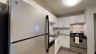 This single-floor residence offers a clean, modern aesthetic throughout its thoughtfully designed layout. The kitchen is a standout feature, showcasing white shaker-style cabinetry, granite countertops, a classic white subway tile backsplash, stainless steel appliances including a refrigerator and range, and wood-look flooring that ties the space together with a contemporary feel. A dedicated dining area adjacent to the kitchen features dark wood-look flooring and a pendant light fixture, providing a functional and stylish space for meals. The living room is bright and open, with sliding glass doors that invite natural light and provide direct access to an outdoor patio area. Two well-sized bedrooms feature plush carpeting, windows with blinds, and built-in closets offering ample storage. The two bathrooms are consistently finished with white shaker vanities, granite countertops, and wood-look flooring. One bathroom includes a tiled tub-and-shower combination with clean white tile surround. Neutral wall tones and textured ceilings are consistent throughout, contributing to a cohesive and move-in-ready atmosphere across the entire residence.